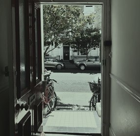 A view of a street from inside a house's door. The image is nearly monochrome.